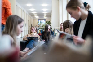 Grupė jaunų žmonių sėdi universiteto erdvėse ir šnekučiuojasi