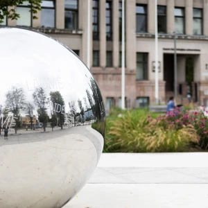 Kauno technologijos universiteto centriniai rūmai – istorinės architektūros pastatas su kolonomis, priekyje matoma aikštė ir žaliuojantys medžiai, saulėta diena.