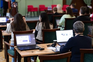 Grupė žmonių sėdi studijų auditorijoje prie kompiuterių