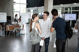3 jaunuoliai šnekučiuojasi universiteto erdvėse