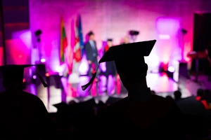 Magistro išankstinis priėmimas Lietuvoje 2026. Nuotraukoje vaikinas iš auditorijos stojasi ir eina link scenos atsiimti magistrantūros diplomo.