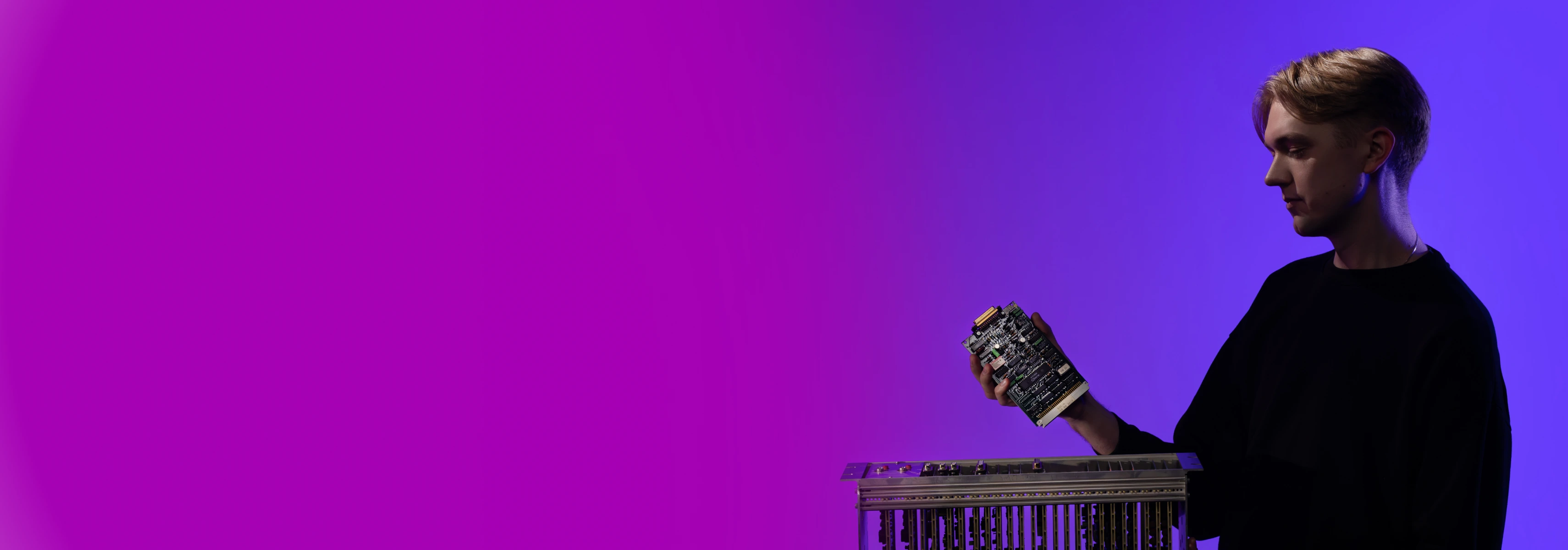 Studentas violetiniame fone rankose laiko elektroninę plokštę, tinkamą informatikos fakulteto veikloms.