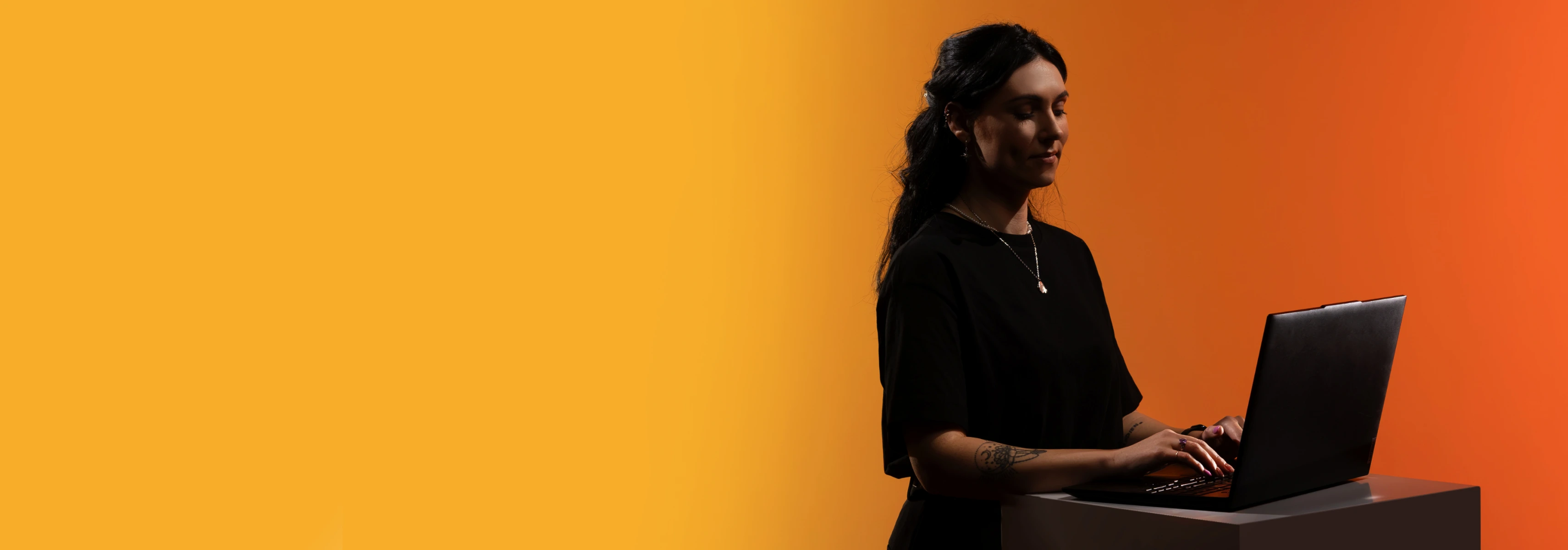 Studentė oranžiniame fone dirba su nešiojamuoju kompiuteriu, tinkamu matematikos ir gamtos mokslų fakulteto užsiėmimams.