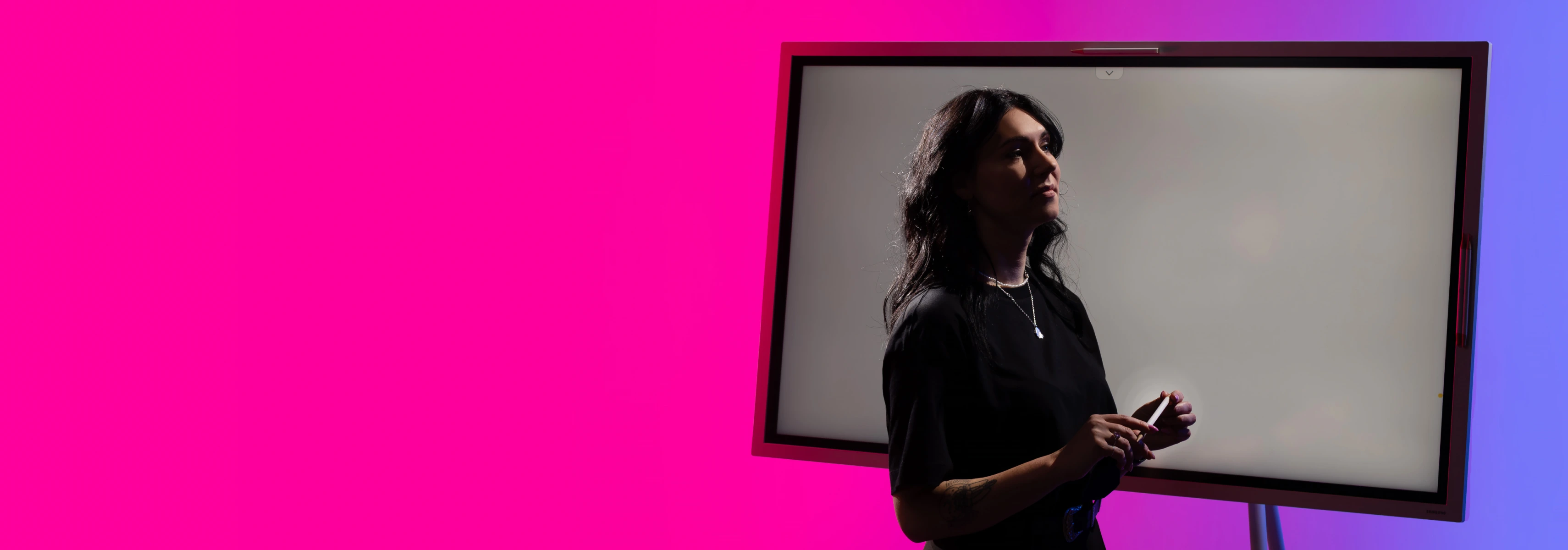 Dėstytoją stilizuotame fone stovi šalia baltos rašymo lentos, galimai ruošiasi paskaitoms fakultete.