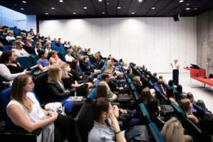 Nuotraukoje matoma dėstytoja vedanti paskaitą pilnai studentų auditorijai, rodanti, jog KTU socialinių, humanitarinių ir menų krypčių bakalauro studijos yra perspektyvios.