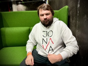KTU mokslininkas B. G. Urbonavičius pozuoja su Jonavos miesto džemperiu, fone matosi žalias fotelis